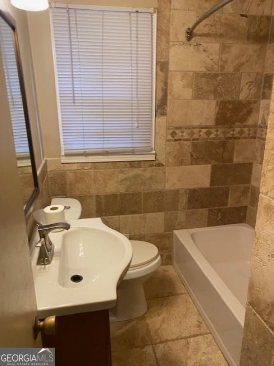 full bathroom featuring tile walls, toilet, tiled shower / bath combo, vanity, and tile floors