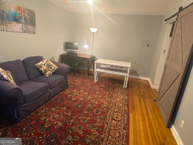 living room featuring wood-type flooring, lofted ceiling, ceiling fan, and a barn door