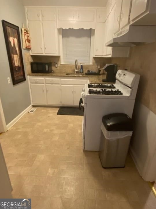 kitchen featuring white gas range oven, sink, light tile floors, and white cabinetry