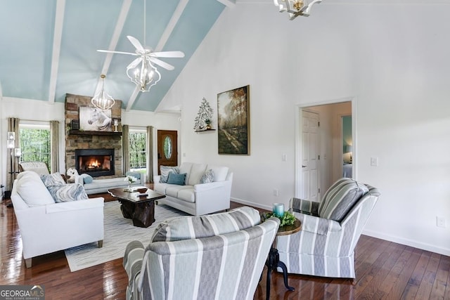 living room with a stone fireplace, high vaulted ceiling, ceiling fan with notable chandelier, dark hardwood / wood-style flooring, and beam ceiling