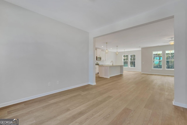 unfurnished living room with ceiling fan, sink, and light wood-type flooring