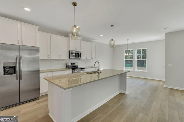 kitchen with appliances with stainless steel finishes, white cabinetry, sink, hanging light fixtures, and a center island with sink