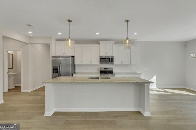 kitchen featuring light stone countertops, appliances with stainless steel finishes, a kitchen island with sink, and white cabinets