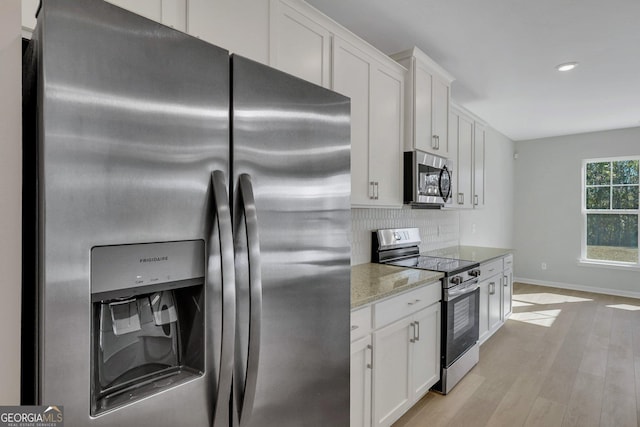 kitchen with light stone counters, light wood-type flooring, appliances with stainless steel finishes, white cabinets, and backsplash