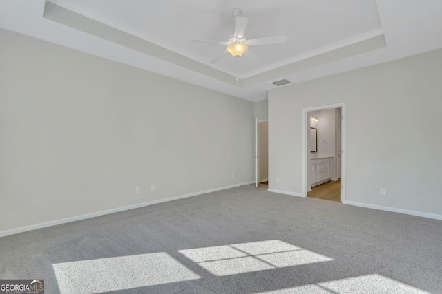 unfurnished bedroom featuring ceiling fan, light colored carpet, a raised ceiling, and ensuite bath