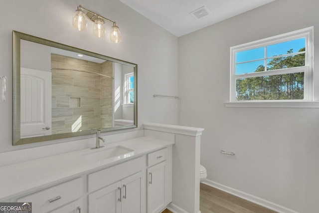 bathroom with hardwood / wood-style flooring, vanity, toilet, and a tile shower