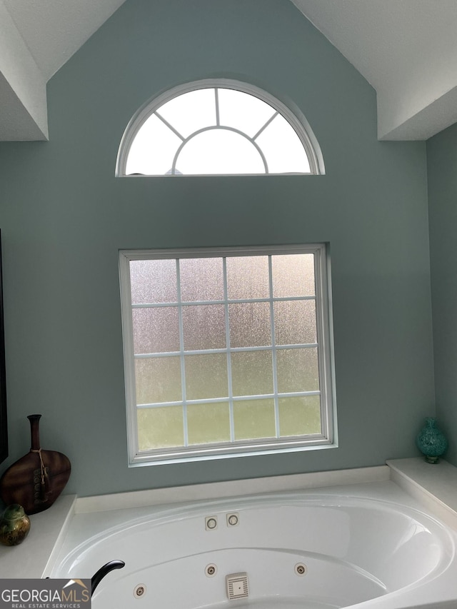 bathroom with a tub to relax in, vaulted ceiling, and plenty of natural light