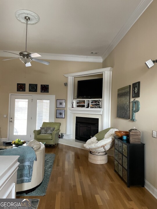 living room featuring wood-type flooring, crown molding, and ceiling fan