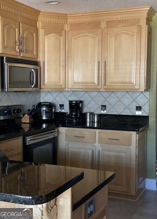 kitchen with tasteful backsplash, tile patterned floors, appliances with stainless steel finishes, and a textured ceiling