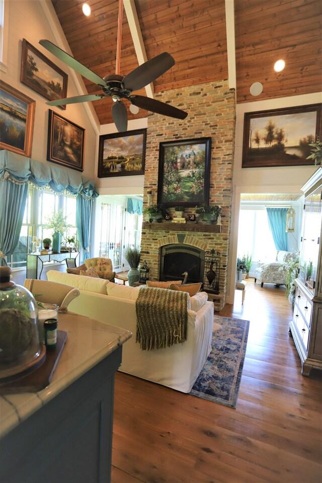 living room with ceiling fan, a stone fireplace, high vaulted ceiling, wooden ceiling, and dark hardwood / wood-style flooring