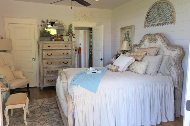 bedroom featuring wooden walls, dark wood-type flooring, and ceiling fan