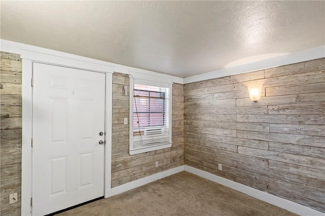 carpeted foyer entrance featuring a textured ceiling and wood walls