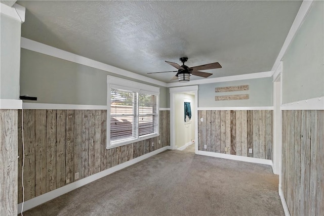 carpeted empty room featuring wooden walls, ceiling fan, and a textured ceiling