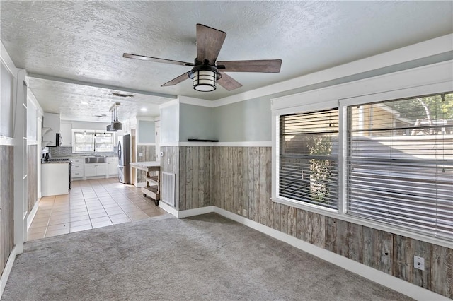 unfurnished room featuring light carpet, a textured ceiling, and wooden walls