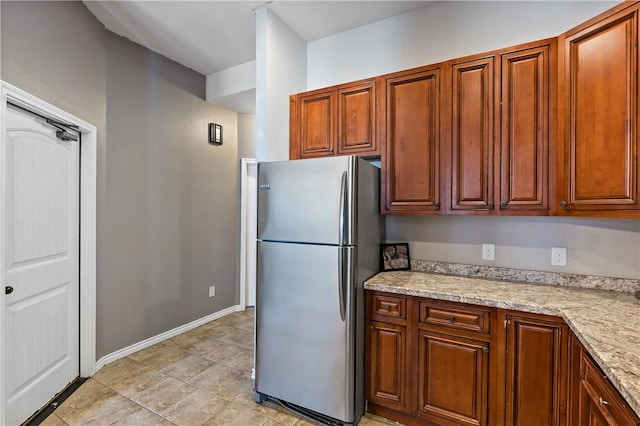 1205 Carolina St, College Station, TX 77840 - kitchen with light stone counters, freestanding refrigerator, brown cabinetry, and baseboards