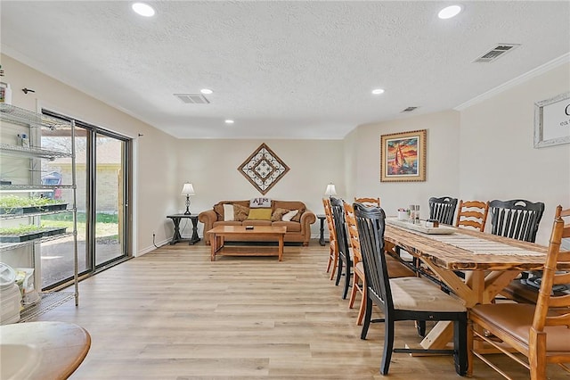 dining area featuring crown molding, light wood-type flooring, and a textured ceiling