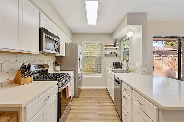 kitchen featuring light wood-type flooring, tasteful backsplash, stainless steel appliances, sink, and white cabinets