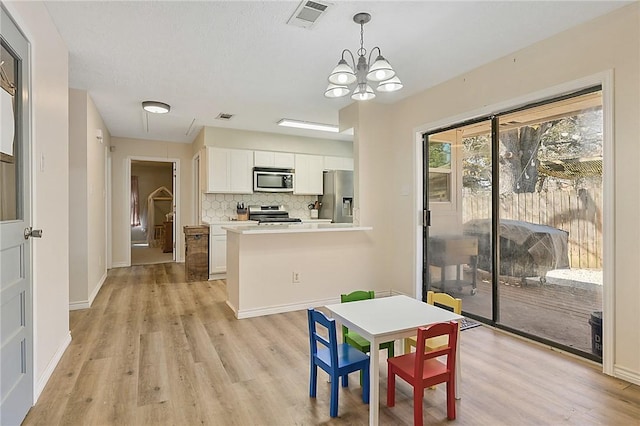 kitchen featuring white cabinetry, hanging light fixtures, stainless steel appliances, light hardwood / wood-style floors, and decorative backsplash