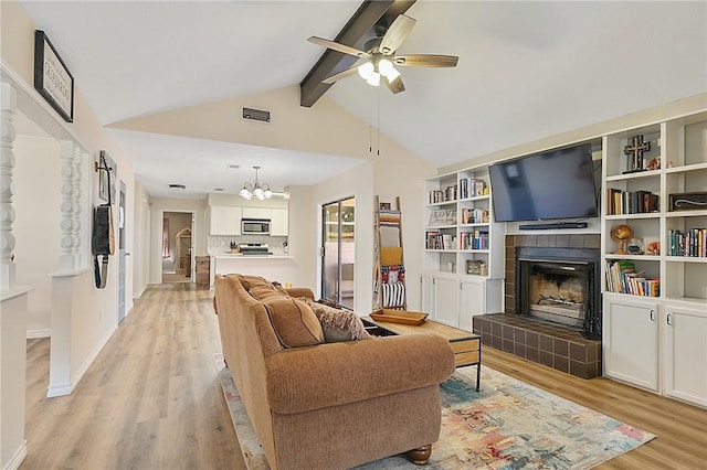 living room with ceiling fan with notable chandelier, vaulted ceiling with beams, light hardwood / wood-style floors, and a tiled fireplace