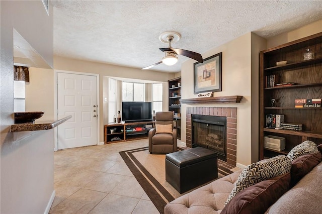 living room with a textured ceiling, a ceiling fan, built in features, a brick fireplace, and tile patterned floors