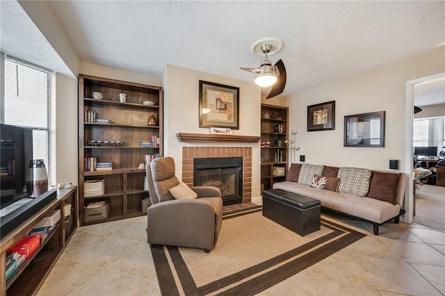 living area featuring a ceiling fan, a fireplace, a textured ceiling, and light tile patterned floors