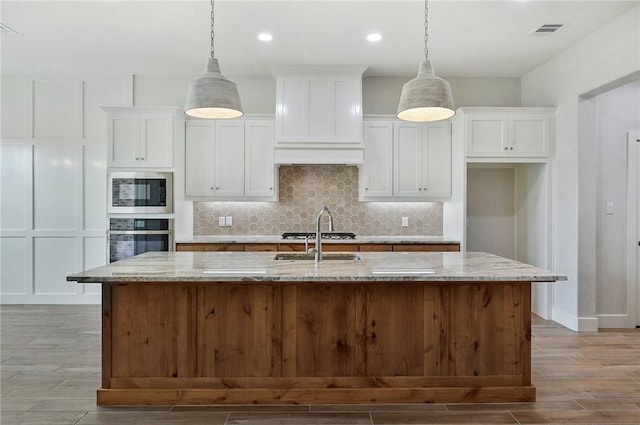 kitchen with light stone counters, a center island with sink, white cabinets, and appliances with stainless steel finishes