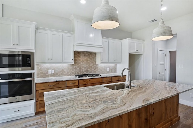 kitchen with stainless steel appliances, a kitchen island with sink, and hanging light fixtures