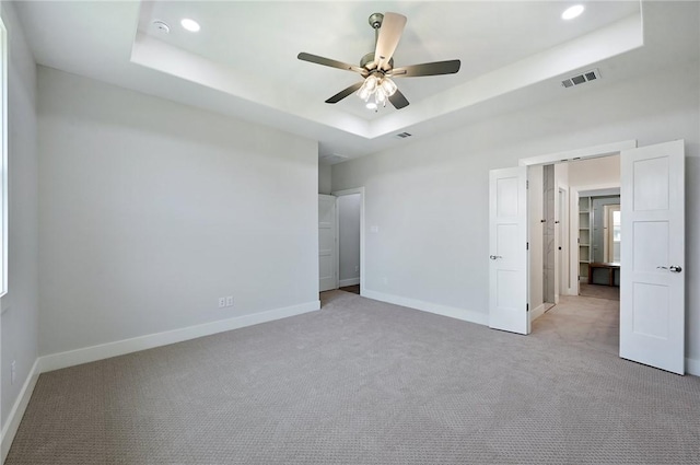 unfurnished bedroom with light carpet, a raised ceiling, and ceiling fan