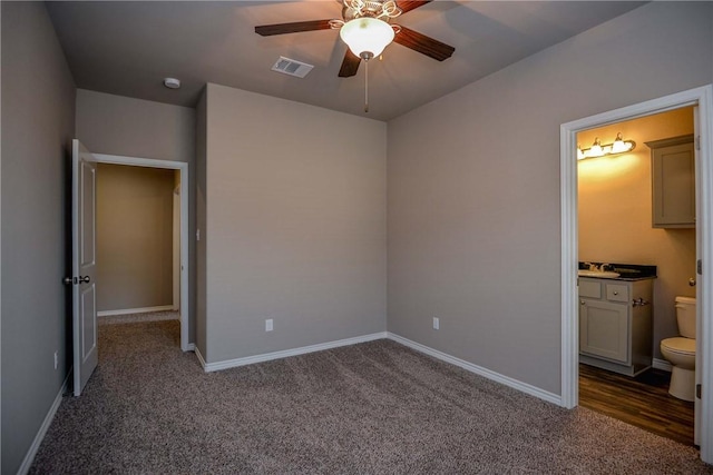 unfurnished bedroom featuring dark colored carpet, ensuite bathroom, and ceiling fan