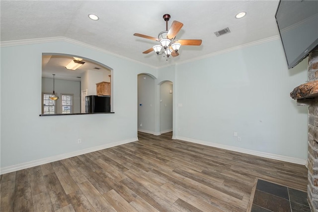 unfurnished living room with arched walkways, ornamental molding, wood finished floors, and visible vents