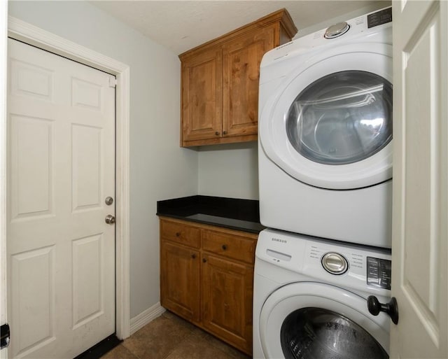 clothes washing area featuring cabinet space, stacked washer / drying machine, and dark tile patterned flooring