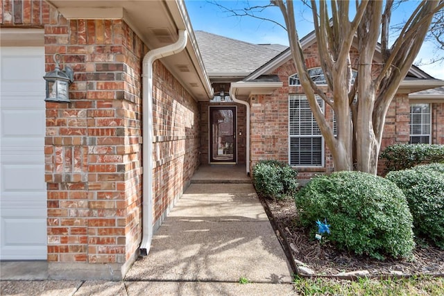 entrance to property with brick siding, roof with shingles, and an attached garage