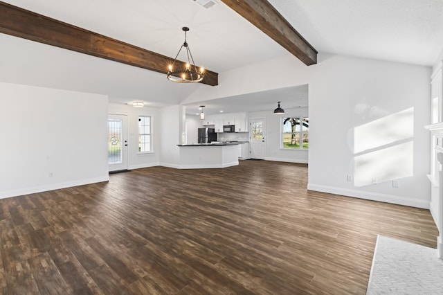 unfurnished living room with a wealth of natural light, dark wood-type flooring, lofted ceiling with beams, and an inviting chandelier