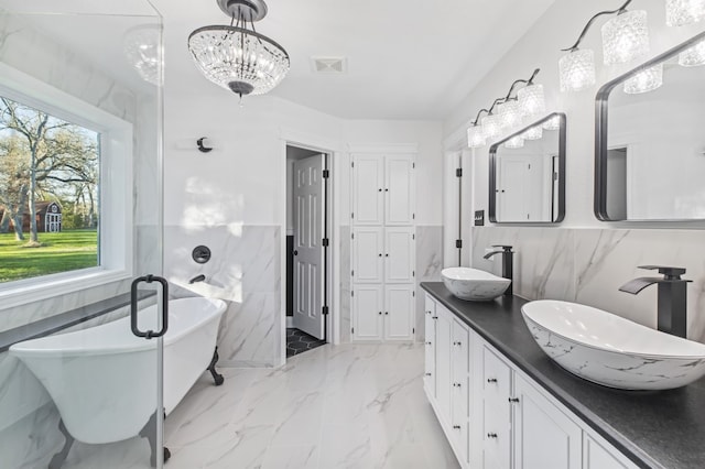 bathroom with a chandelier, vanity, tile walls, and a tub