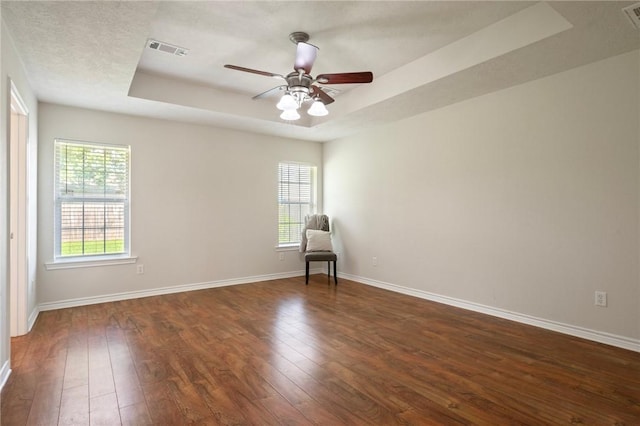 empty room with dark wood-style flooring, a raised ceiling, baseboards, and visible vents