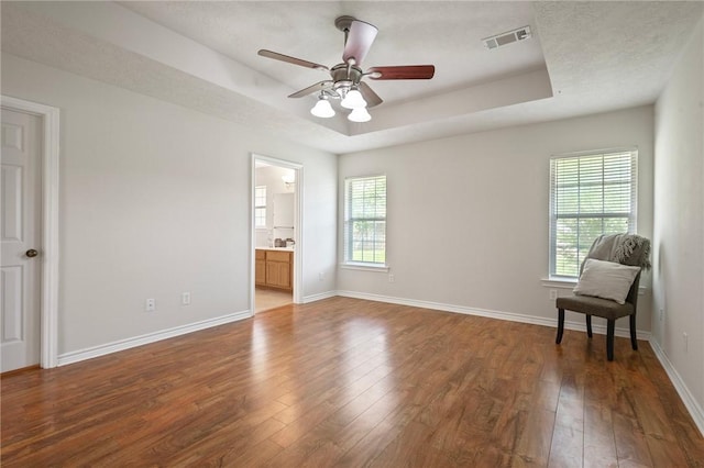 unfurnished bedroom featuring a tray ceiling, wood-type flooring, baseboards, and visible vents