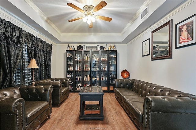 living room with hardwood / wood-style flooring, ceiling fan, ornamental molding, and a tray ceiling