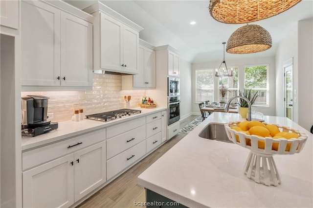 kitchen with light wood-type flooring, backsplash, stainless steel appliances, decorative light fixtures, and white cabinets