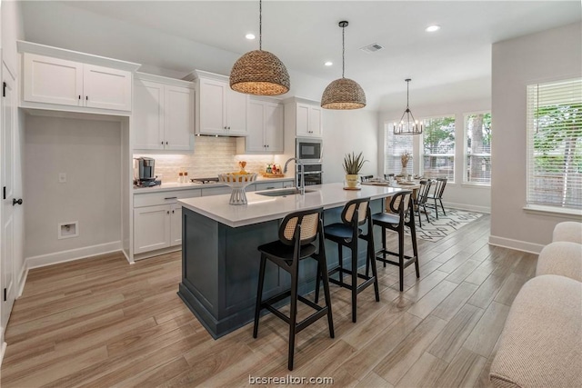 kitchen featuring a center island with sink, white cabinets, stainless steel appliances, and hanging light fixtures