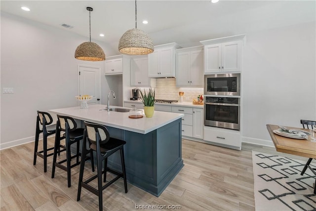 kitchen with appliances with stainless steel finishes, white cabinetry, pendant lighting, and an island with sink