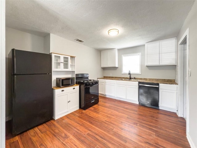 kitchen with white cabinets, a sink, visible vents, black appliances, and dark wood finished floors
