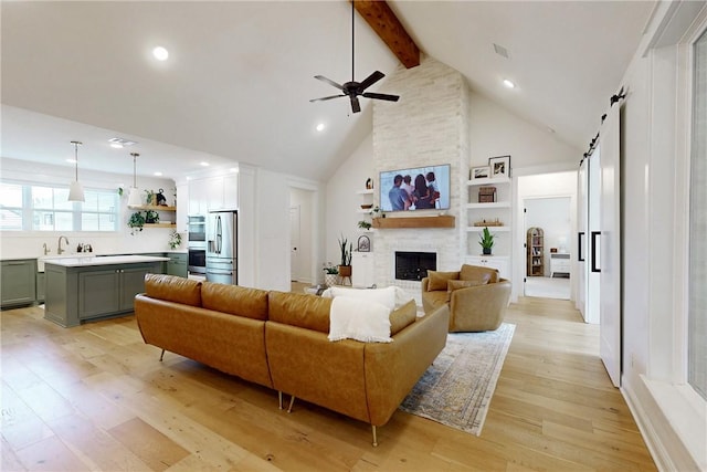 living area with high vaulted ceiling, beam ceiling, a barn door, ceiling fan, and light wood-style floors