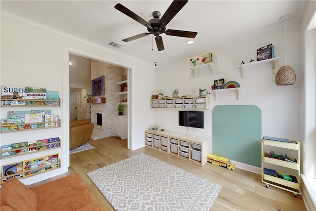 playroom with crown molding, a fireplace, ceiling fan, and wood finished floors