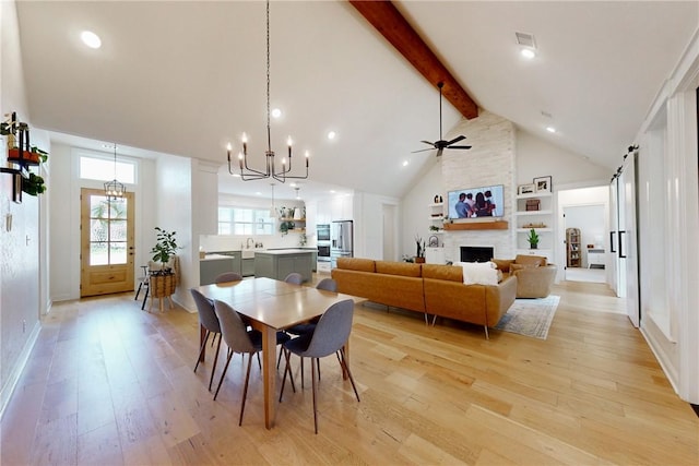 dining space featuring light wood-style flooring, ceiling fan with notable chandelier, high vaulted ceiling, beam ceiling, and a large fireplace
