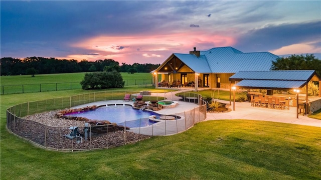 pool at dusk featuring a patio, pool water feature, an outdoor bar, and a lawn