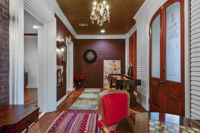 entrance foyer with a chandelier, crown molding, brick wall, and french doors