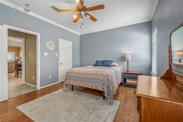 bedroom featuring a ceiling fan, wood finished floors, visible vents, baseboards, and crown molding