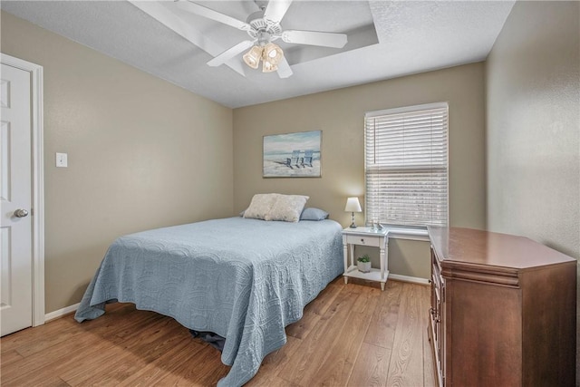 bedroom with ceiling fan, baseboards, a textured ceiling, and light wood-style flooring