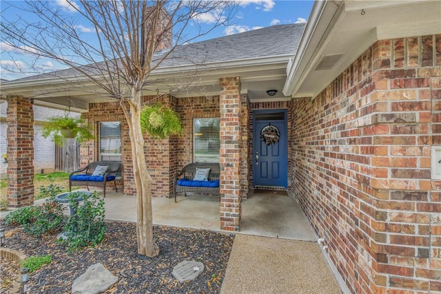 entrance to property with a porch, brick siding, and roof with shingles