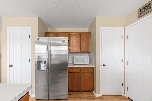 9939 County Road 272, Somerville, TX 77879 - kitchen with stainless steel fridge, white microwave, light wood finished floors, and brown cabinetry